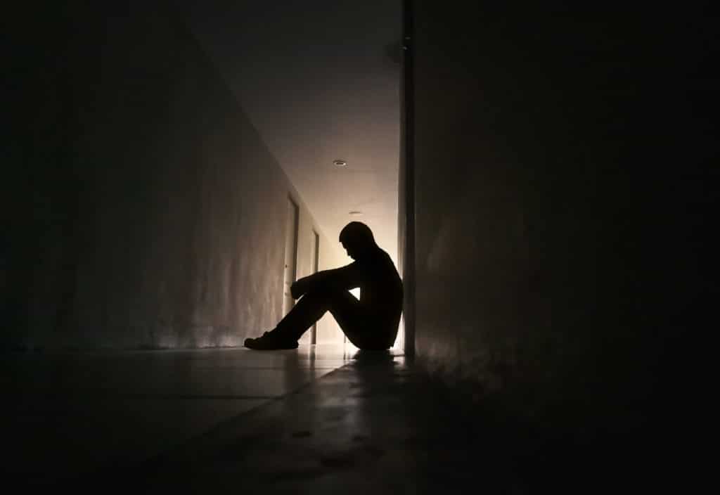 Silhouette Of Depressed Man Sitting On Walkway Of Residence Building.