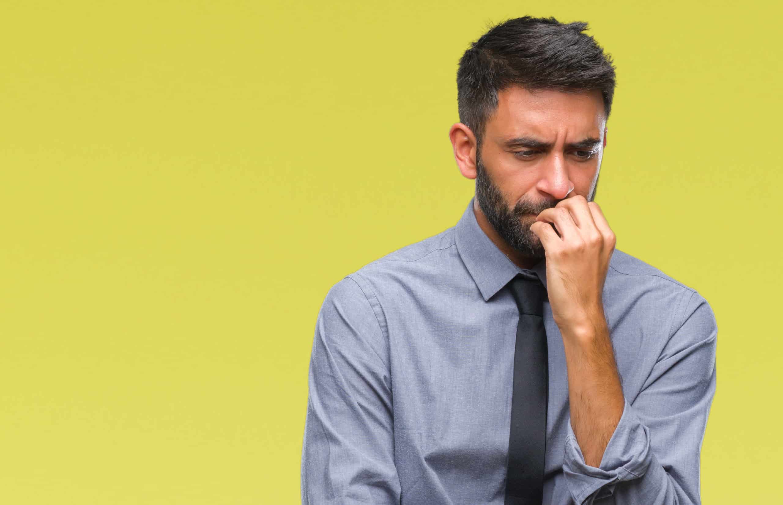 Adult Hispanic man looking stressed ahdn standing near yellow background