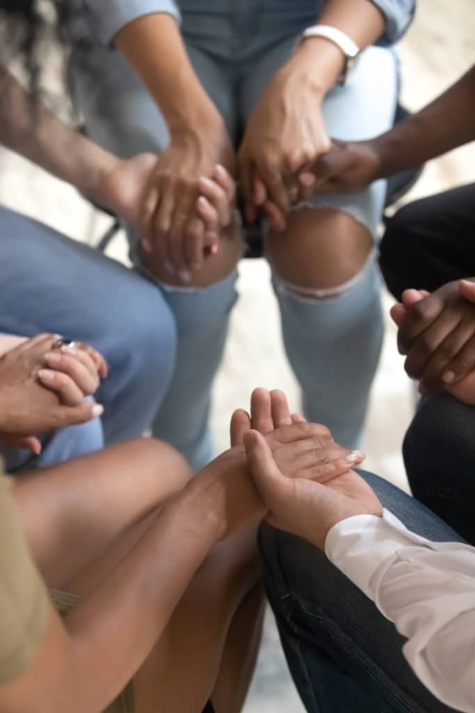Close Up Vertical View of Diverse People Sitting On Chairs holding hands