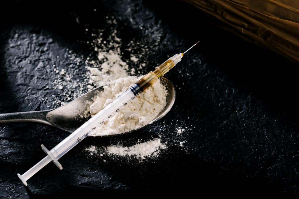 Heroin In A Syringe And Heroin Powder On A Black
