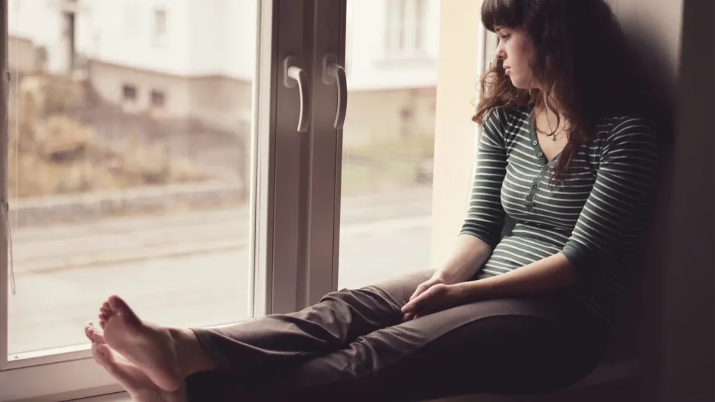 Teen sitting at window looking over the house as if she is suffering from depression.