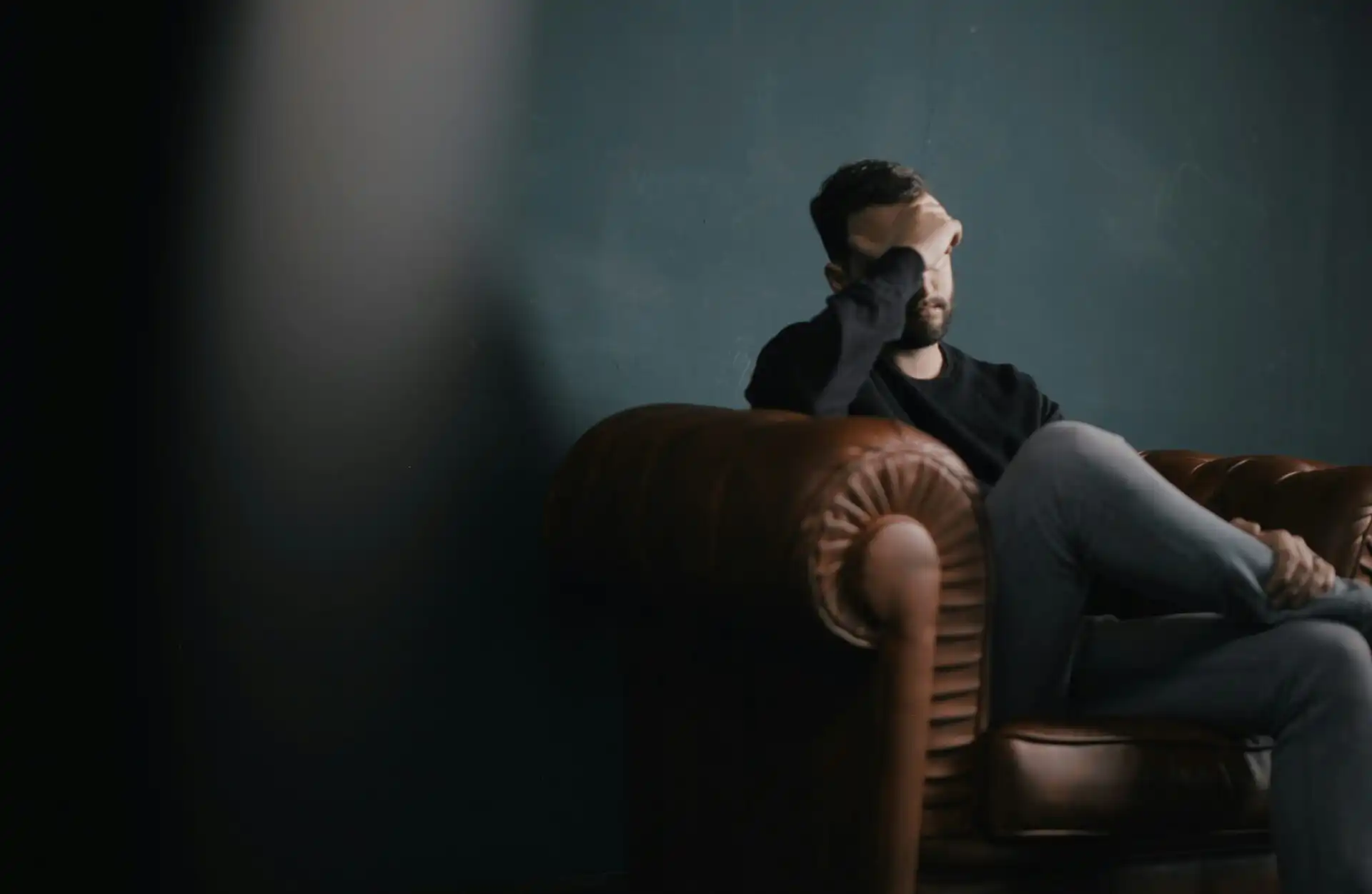 man sitting on a sofa with his hand covering his face